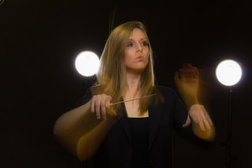 Young caucasian woman conductor gestures with baton and leaves light trails