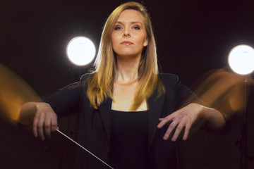 Young caucasian woman conductor gestures with baton and leaves light trails