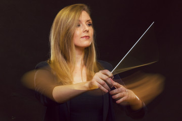 Young caucasian woman conductor gestures with baton and leaves light trails