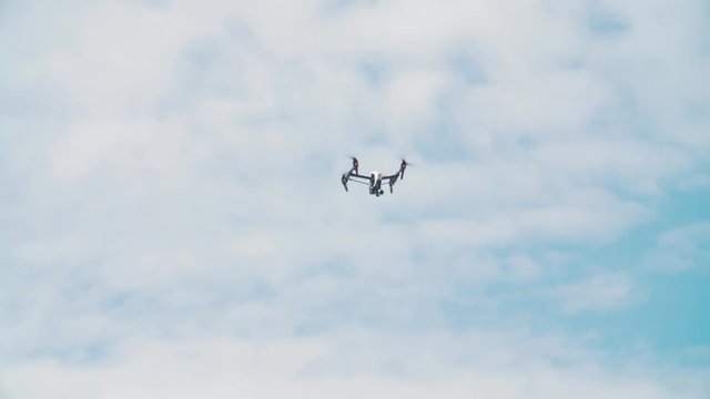 Filming white quadrocopter flying in front of blue sky white clouds on summer sunny day