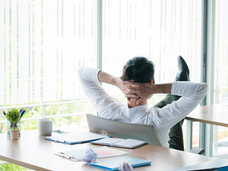 Businessman relaxing concept: businessman sitting with feet up at office desk looking out of window...