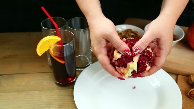 On a wooden table, a woman breaks a pomegranate by her own hands,. Hd shot with dolly .The camera moves from left to right