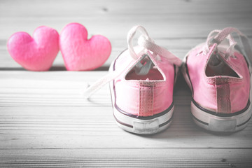 Pink girl's sneakers with pink hearts on a wooden floor, selective color