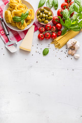 Italian food cuisine and ingredients on white concrete table. Spaghetti Tagliatelle olives olive oil tomatoes parmesan cheese garlic pepper and basil leaves and checkered tablecloth.