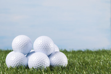 Many golf balls lie on the green grass against the blue sky