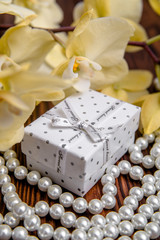 Gift box on a background of yellow orchids and pearls 