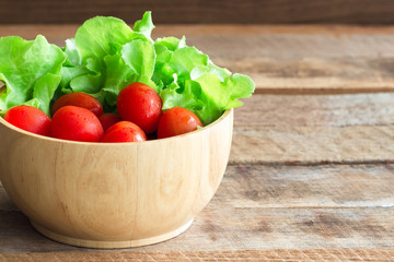 Fresh tomato and lettuce in wood bowl put on wood table. Side view of tomato and green oak lettuce with copy space for background. Fresh green oak lettuce and tomato prepare for cooking.