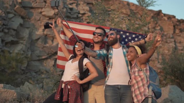 Slow motion of multiracial group of friends posing with backpacks and American flag taking selfie on nature.