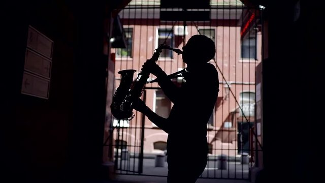 black silhouette of a young musician saxophonist. play a wind musical instrument on the street in the tunnel. plays jazz