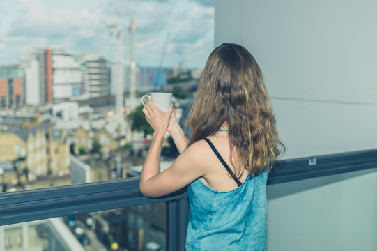 Woman with cup of coffee on balcony in city