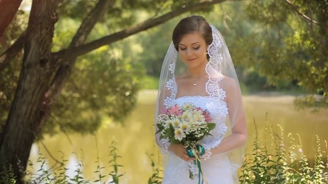 Beautiful bride stands near the lake and waits for the groom