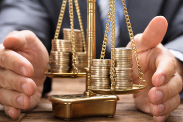 Businessman Covering Stacked Coins On Weighing Scale