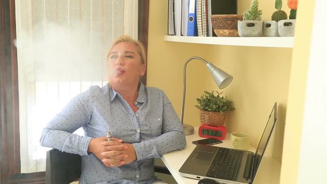 Portrait of attractive blonde woman  smoking electronic cigarette at home interior