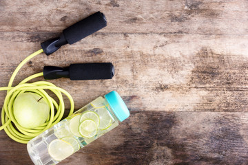jumping rope, detox lime drink in bottle and green apple on wooden table