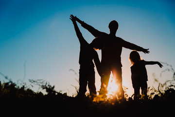 father with son and daughter silhouettes play at sunset