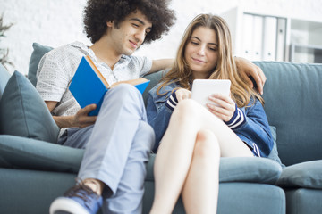 Young people sitting at couch with a tablet and a book