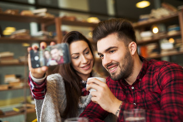 Young happy couple is making a selfie in a cafe.