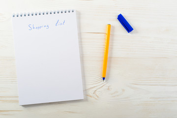 shopping list phrase in notepad with pen on light wooden table, top view, copyspace for text