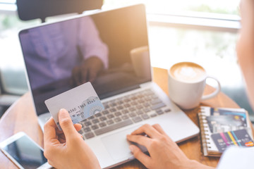 A woman's hand holds a credit card and uses  a  laptop computer to shop online.
