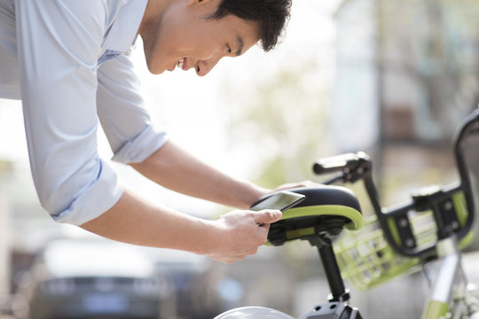 Young man scanning a QR code to unlock a share bike