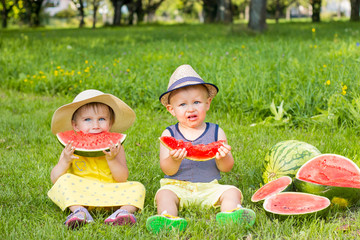 Cute little boy and little girl sitting on grass and eating watermelon. Summer fruits.