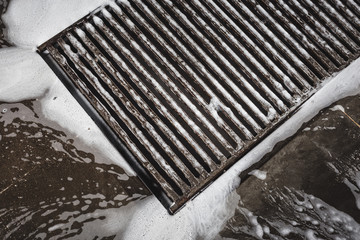 Water drainage grill on the car wash, foam flowing into the sink