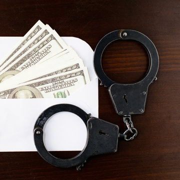 close-up the envelope with dollars money and steel police handcuffs on wooden table, top view. Concept of bribery