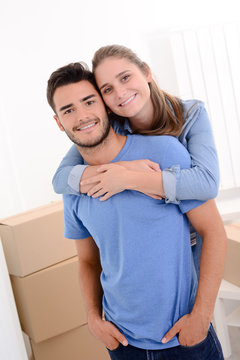 portrait of lovely cheerful young couple posing in their new home while moving apartment cardboard boxes background