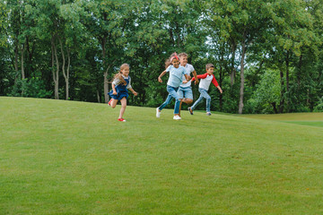 Happy multiethnic kids playing together and running on green grass in park