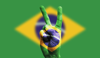 Brazil national flag painted onto a male hand showing a victory, peace, strength sign