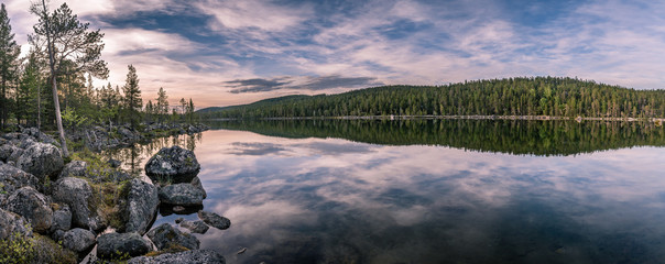 Panorama of calm lake at Lapland in midnight sun time. Rocks in front.