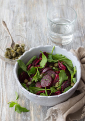 Beetroot salad with baked red onion, capers, watercress, greens and vinaigrette sauce. Vegan healthy food. In a blue bowl on a wooden table