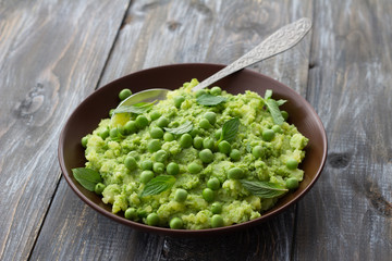 Mashed potatoes with green peas, mint and olive oil in a ceramic bowl on a wooden table. Healthy vegetarian food