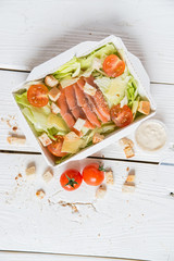 Caesar salad with fish in box on wooden surface