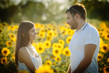 A sweet woman in love looks at her husband, who holds the lady by the hands in the field of the halfpings, the couple is spending a romantic date in nature on a warm summer day