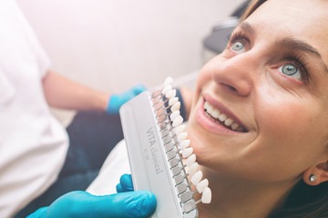 Portrait of a dentist who treats teeth of young woman patient. checking and selecting color of young woman's teeth