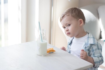 A cute little boy is eating candy and drinking milk. Health. Happy child. Breakfast. A little boy is sitting at the table.
