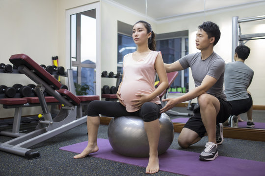 Pregnant woman working with trainer at gym