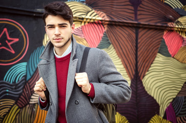 Young fashionable man standing in front of colorful wall. Autumn time outdoors.