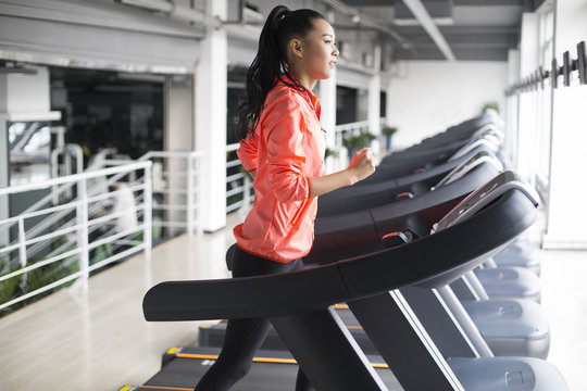 Young woman running on treadmill in gym