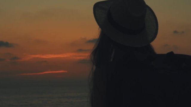 A young sexy woman traveler with a backpack and straw hat on her head makes picture on mobilephone of the sea on sunset and dawn in Cyprus, Silhouette of a girl, close up, 100 frames per second, slow