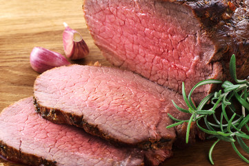 Baked meat, garlic and rosemary on a wooden background. Roast beef.