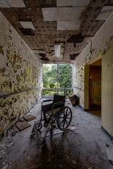 Fototapeta na wymiar Desolate, Deteriorated Hallway with Wheelchair - Abandoned Hospital