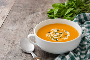 Pumpkin soup in white bowl on wooden table
