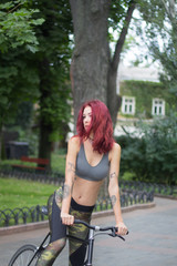 Fototapeta na wymiar Morning bicycle ride of young sexy woman with red hair, sporty female with black bicycle in park 