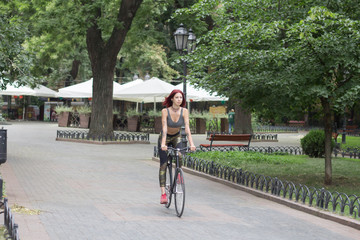 Fototapeta premium Morning bicycle ride of young sexy woman with red hair, sporty female with black bicycle in park