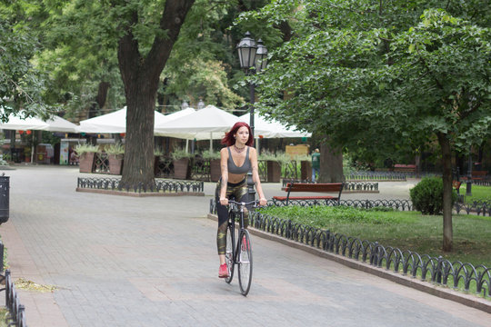 Morning bicycle ride of young sexy woman with red hair, sporty female with black bicycle in park