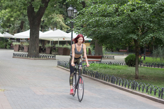 Morning bicycle ride of young sexy woman with red hair, sporty female with black bicycle in park