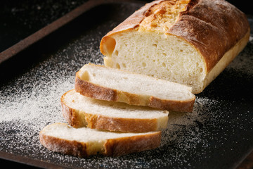 Sliced homemade white wheat bread with wheat flour on old black oven tray as background. Close up