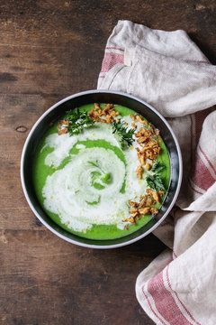 Vegetarian broccoli cream soup served in black bowl with cream, fried onion, fresh parsley, kitchen linen towel over old wooden background. Top view with space. Healthy eating.
